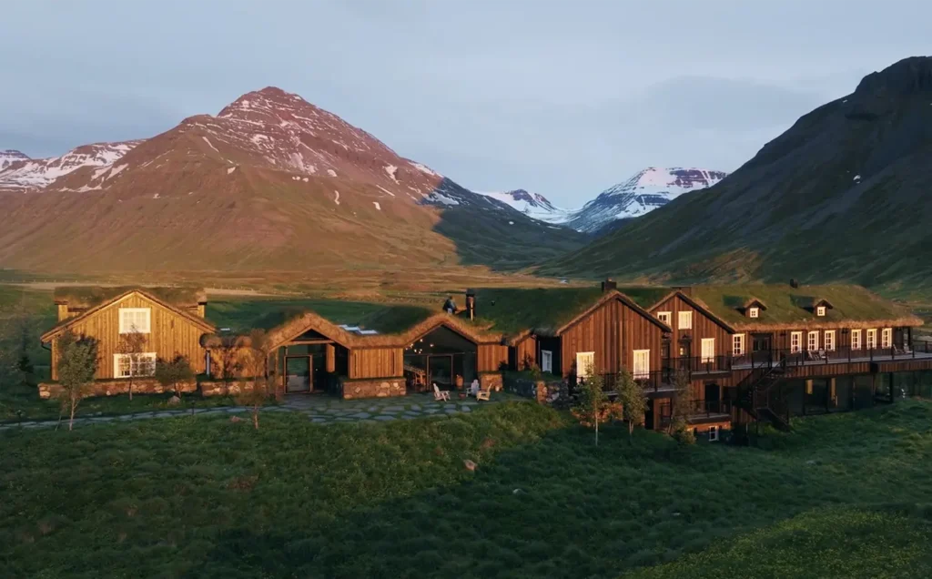 Remote luxury lodge at Deplar Farm in Iceland, surrounded by lush green hills and snowcapped mountains at sunset.